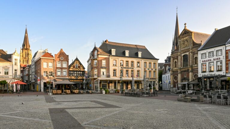Market square in Sittard with historic buildings, café terraces, and church towers surrounding an open paved plaza.